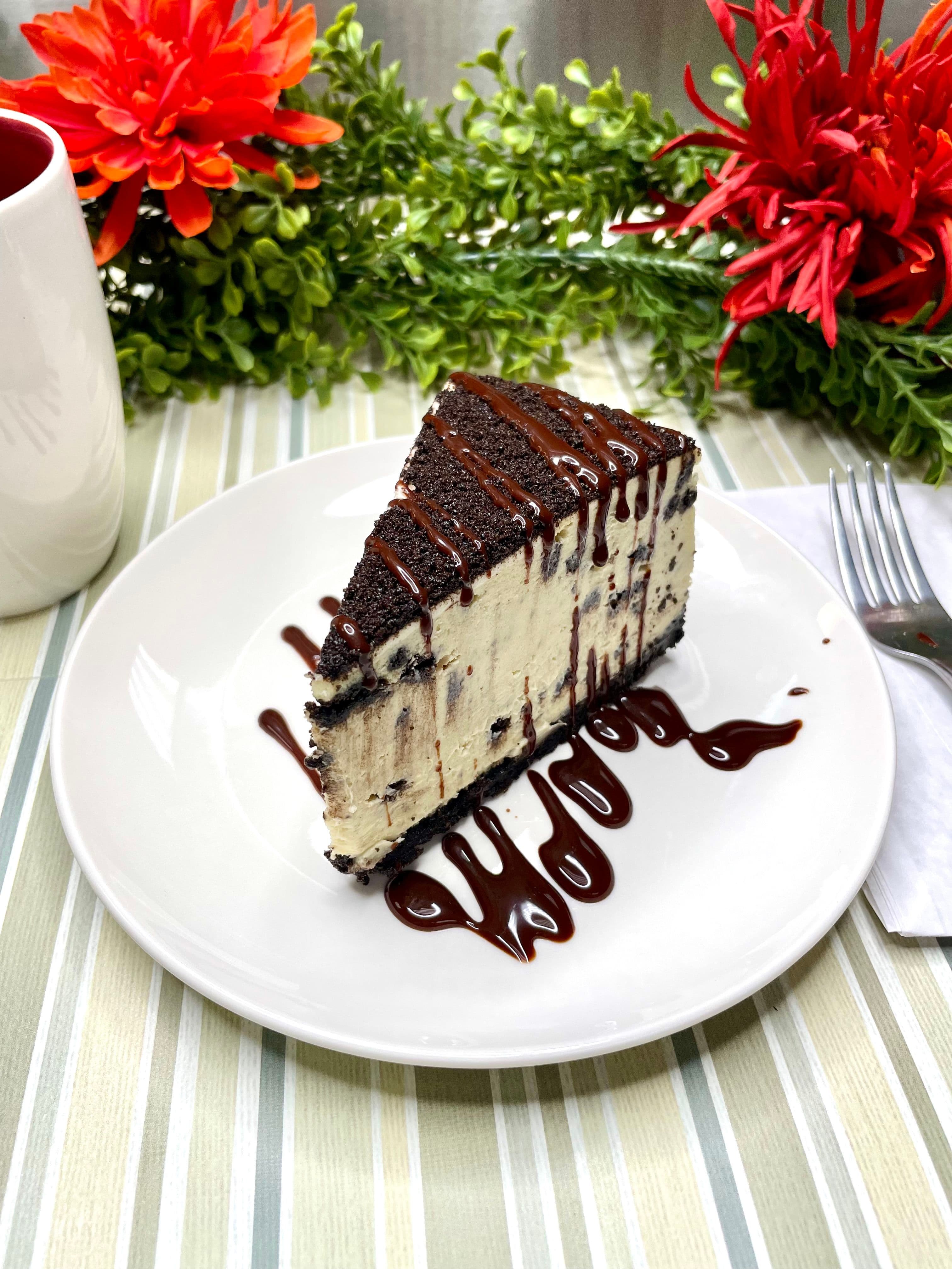 A slice of Oreo cheesecake with a cookie-crumb crust, finished with dark chocolate drizzle.