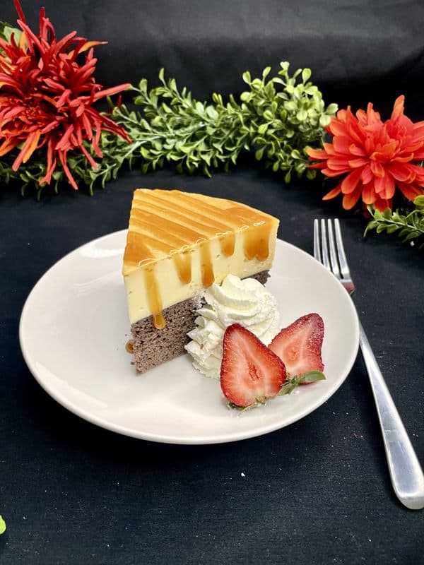 A slice of choco flan — chocolate cake beneath a layer of flan, with whipped cream and a fresh strawberry.