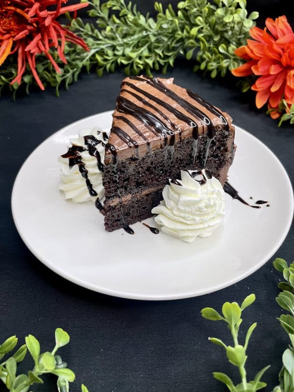 A slice of chocolate layer cake with chocolate drizzle and whipped cream.