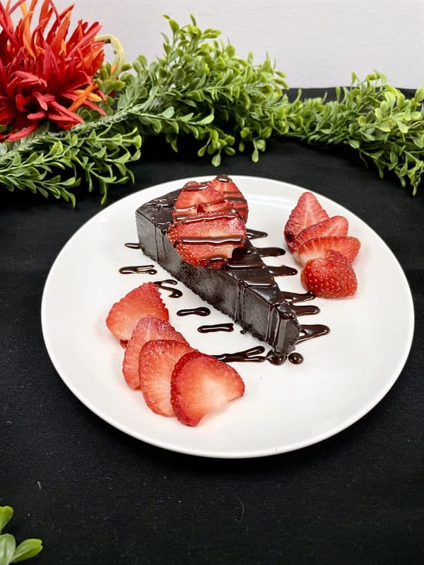 A dark chocolate cheesecake slice served with fresh sliced strawberries.