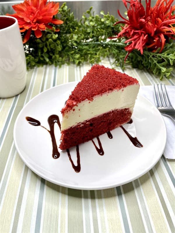 A slice of red velvet cheesecake — red sponge layers around a white cheesecake centre.