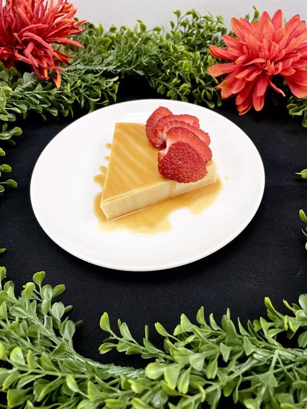 A wedge of flan with caramel sauce and fresh strawberries.