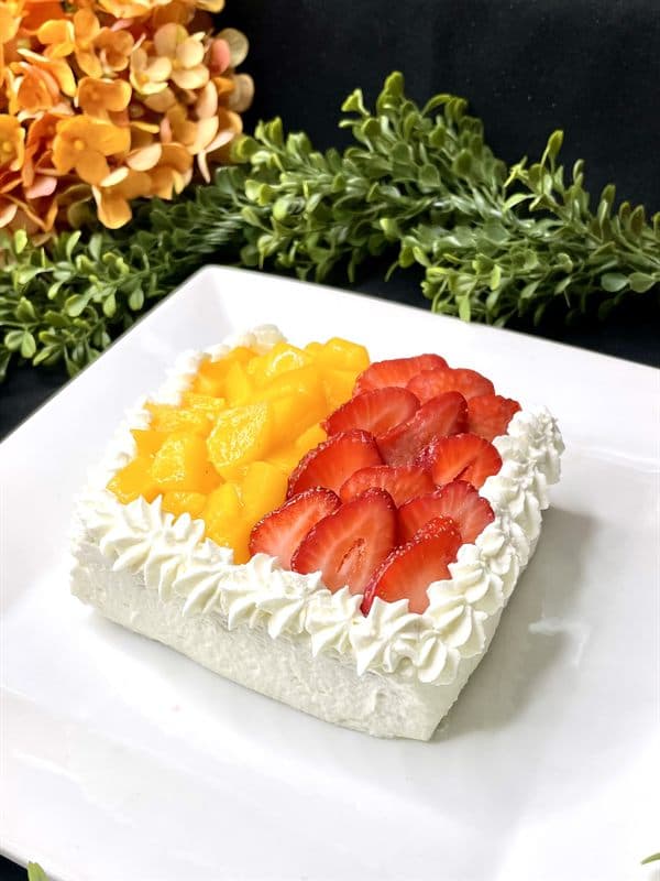 A square slice of tres leches cake piped with whipped cream and topped with mango and strawberries.
