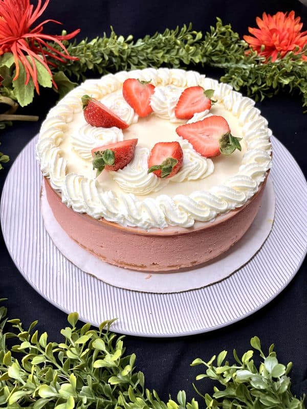 A whole strawberry cheesecake finished with whipped cream and fresh strawberries.