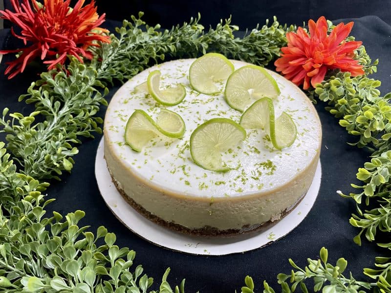 A whole key lime cheesecake topped with fresh lime wheels and lime zest.